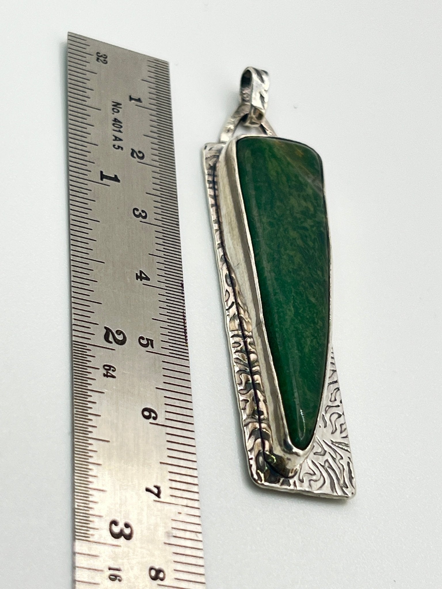 Green stone pendant with silver setting next to a ruler on a white background